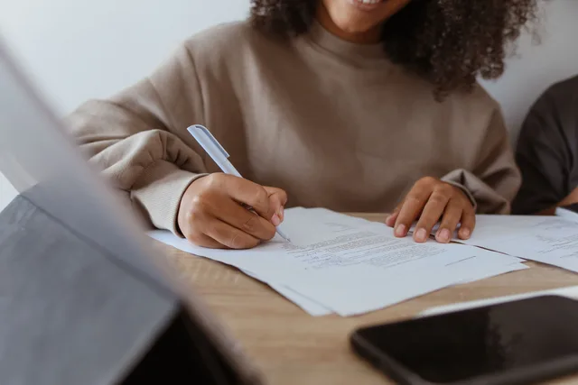 Close-up of a woman's hands writing on documents with a pen indoors. Cross-border casting: pitching US clients from Toronto and Vancouver